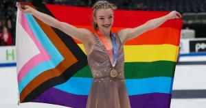 US Figure Skater Amber Glenn holds Progress Pride flag over head after becoming the first out queer woman to win the US Women's Figure Skating Championship.