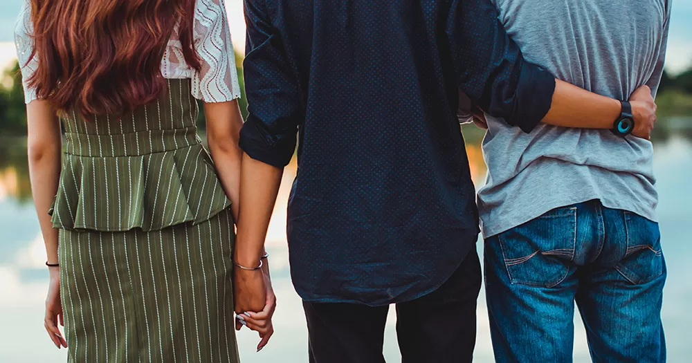 This article is about the referendum to expand the constitutional definition of family. The image shows the backs of three people, who appear to be in a throuple. A woman stands on the left, holding hands with a man in the centre, who also has his arm around another man on his right.