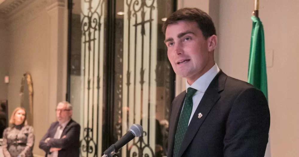 Jack Chambers photographed from the chest up speaking at a podium. He wears a dark grey suit with a green tie.