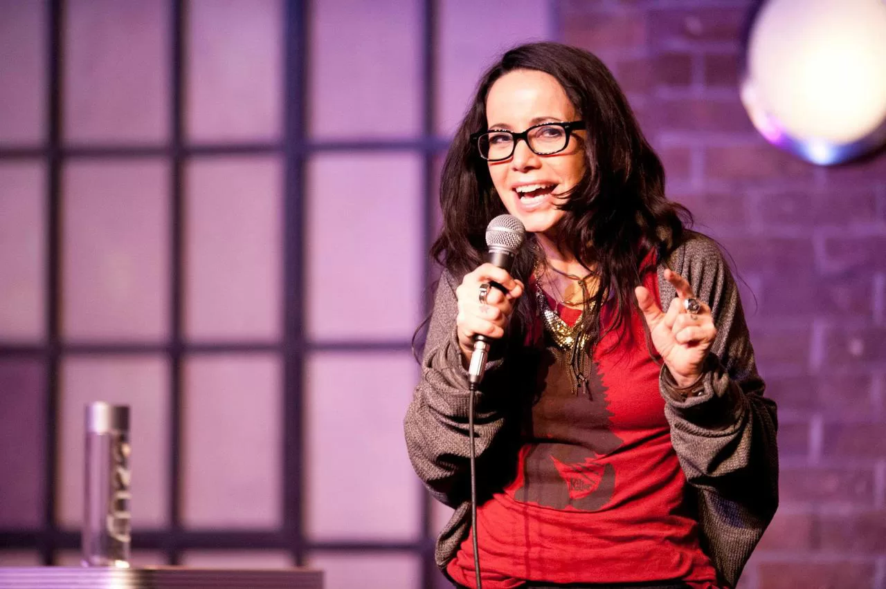 Photo of Janeane Garofalo, one of the asexual celebrities listed in the article, holding a microphone against a purple background