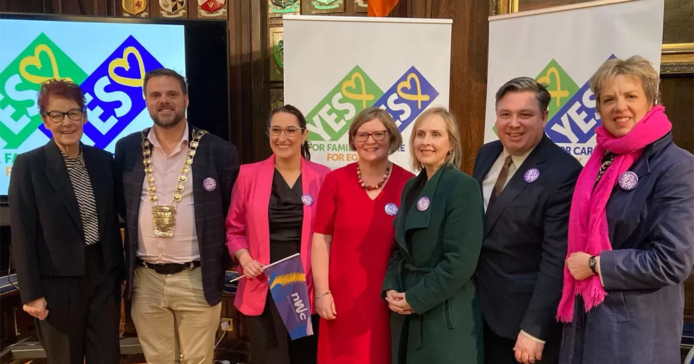 The image shows seven people standing in front of pop up banners that read "YES YES". The image was taken at the National Women's Council of Ireland's launch of the YES YES campaign for the upcoming referendums.