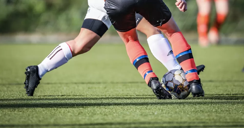 This article is about Sport NI and LGBTQ+ inclusion. In the photo, the legs of two people playing football on a field.