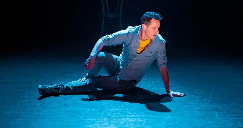 Actor sitting on stage in blue lighting during UNGUARDED production by Anthony Kinahan.