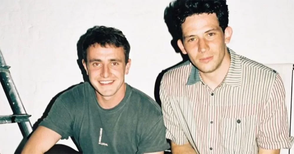 The History of Sound co-stars Paul Mescal and Josh O'Connor. The pair are photographed from the stomach up, looking directly into the camera and smiling.