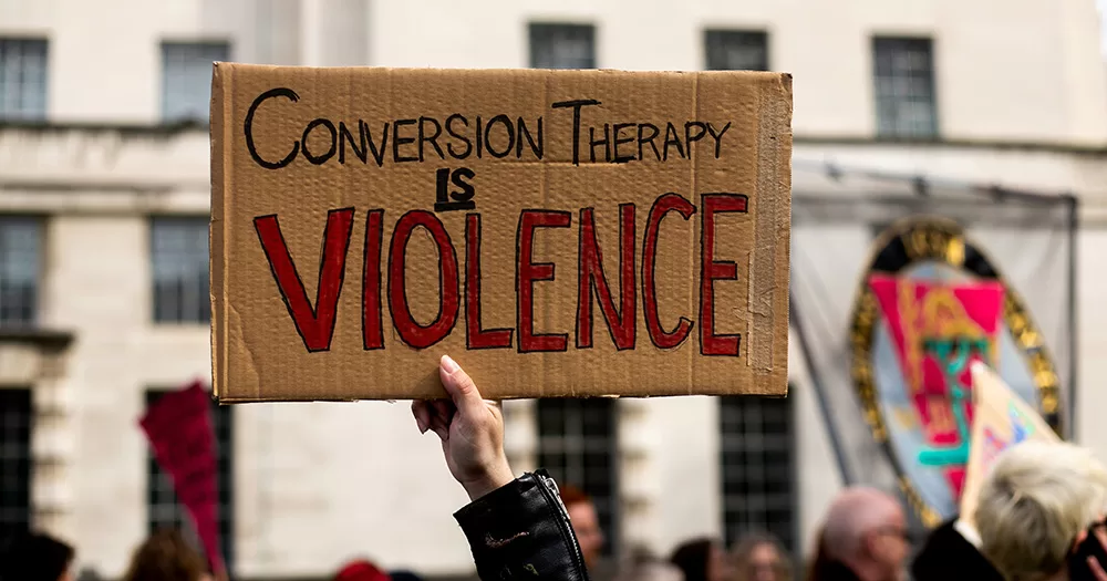 This article is about the Irish conversion therapy bill. The image shows a hand holding a cardboard sign that reads "Conversion therapy is violence".