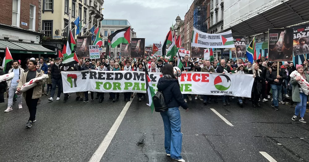 People attending the Palestine solidarity march in Dublin, carrying banners and Palestinian flags in Dame Street.