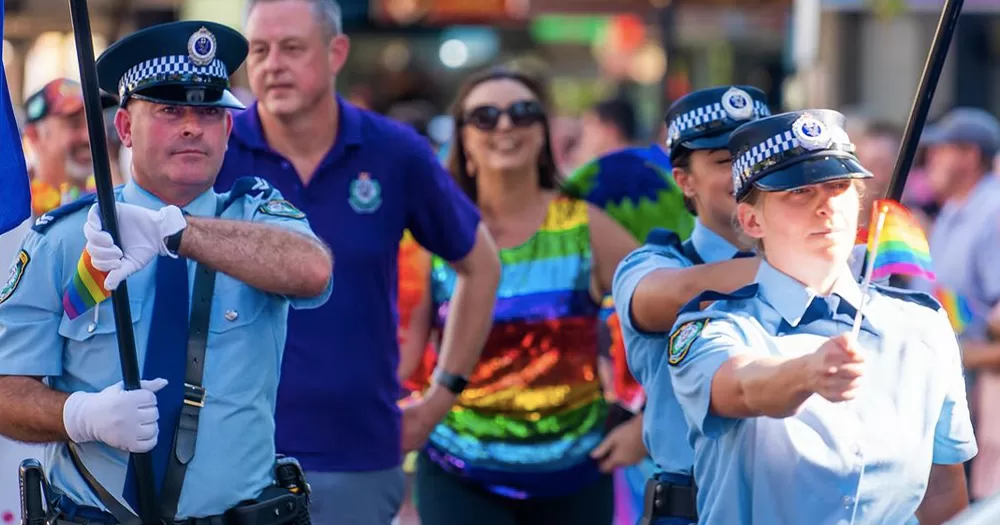 Police marching at Sydney's Mardi Gras, with officers wearing their uniforms and carrying rainbow flags.