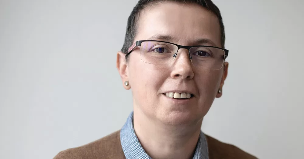 Tran activist Tina Kolos Orban, looking at the camera and smiling in front of a white background.