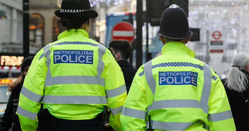 This article is about a stabbing of a trans girl in the Greater London area. The image shows the backs of two Metropolitan Police officers. They were high-vis yellow jackets and black police hats.