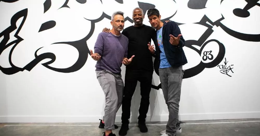 Beastie Boys members Adam Horovitz and Michael Diamond posing in front of a graffiti mural that spells out 'Beastie'.