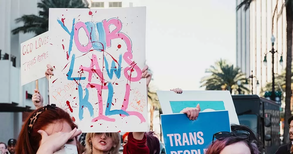 Group of people protesting anti-trans laws with sign that says "your laws kill" the article is about concerns regarding the cass review