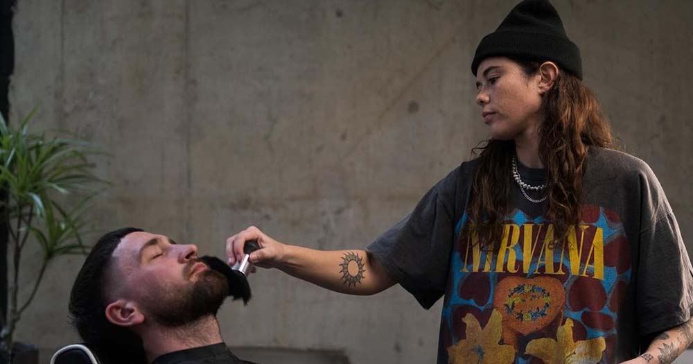 Photo of queer barber Hayden Cassidy standing next to her barbershop client