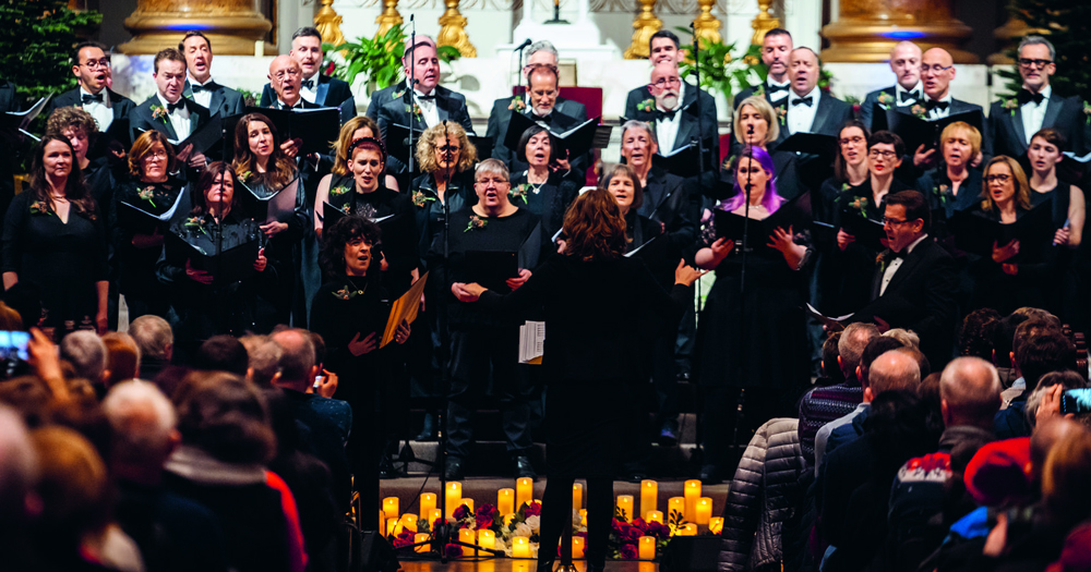 This article is about Glória's Summer Concert. In the photo, the choir Glória singing in a church with the director's back facing the camera.