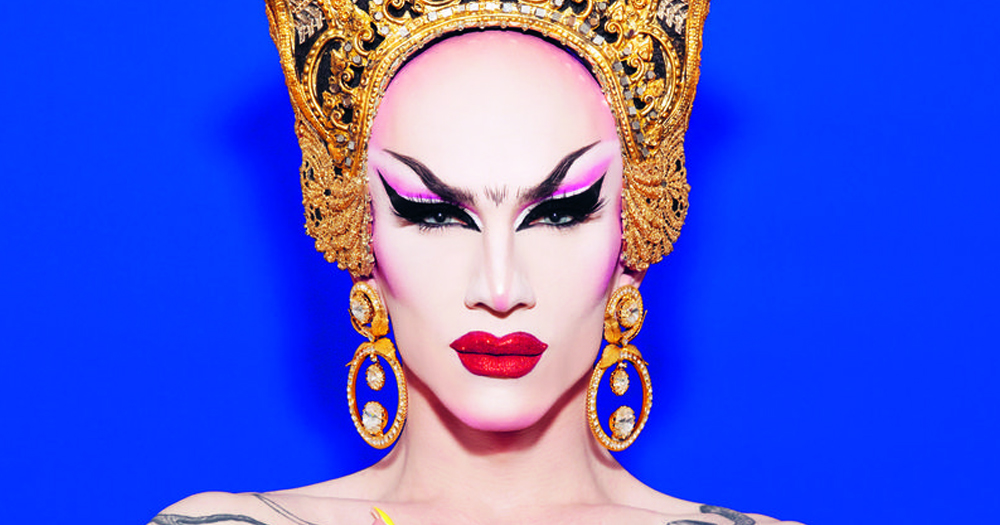 Drag performer Sasha Velour, facing the camera in full drag with a golden headgear in front of an electric blue background.