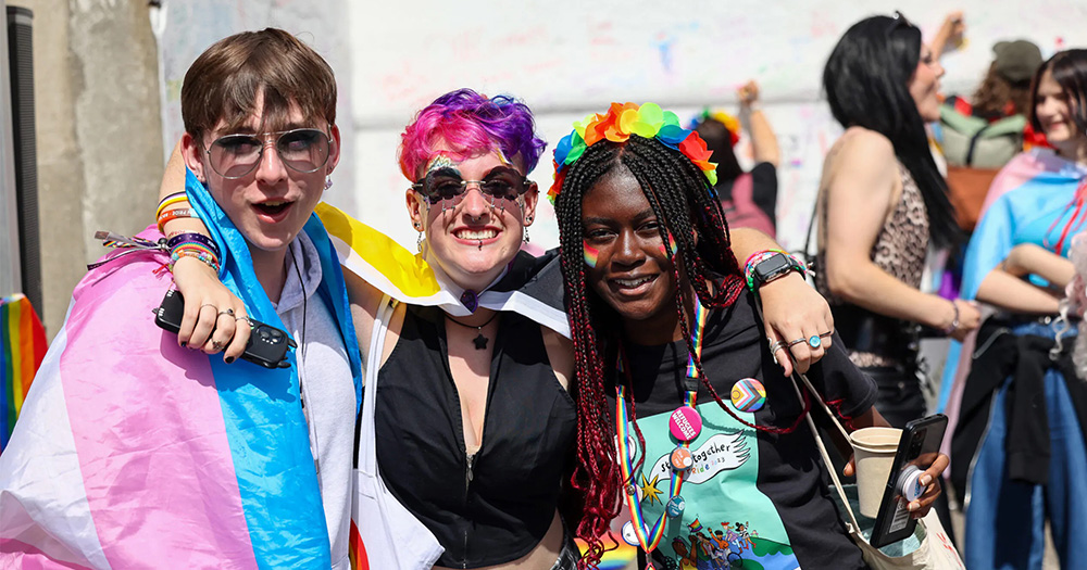 Three young people stand together celebrating Pride.