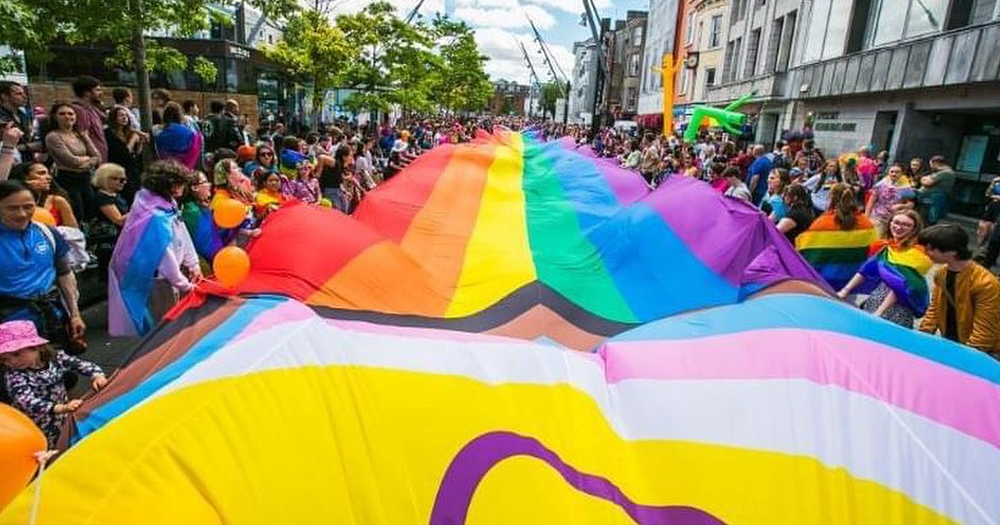 Photo from past Cork Pride, as the organisation prepares for its 2024 festival, showing people holding a massive Pride flag in a street.