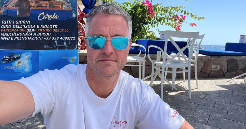 A selfie of Ralf Schumacher. He wears a white t-shirt and sunglasses and smiles slightly at the camera.