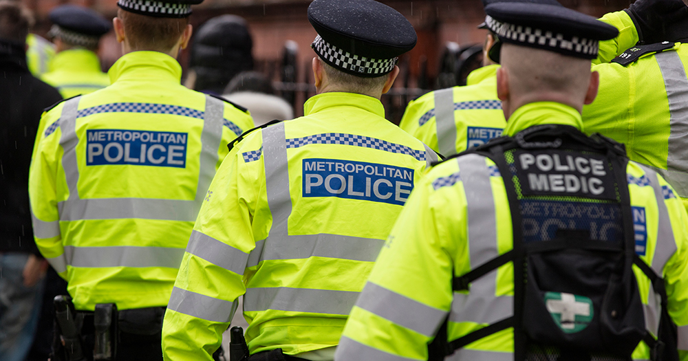 This article is about a suspect being charged with the murder of two men in the UK. In the photo, the backs of police officers from the Metropolitan Police in London in their yellow uniforms.