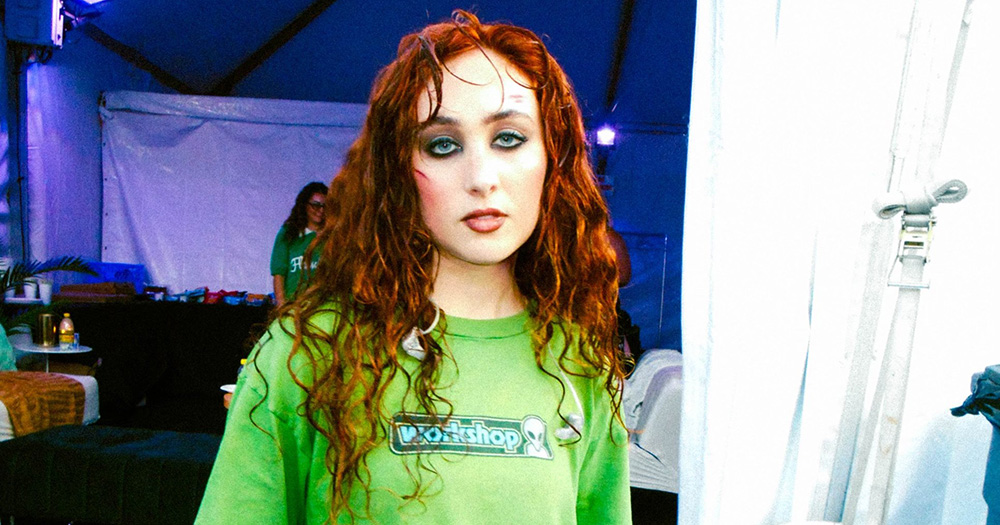 Chappell Roan wears a green t-shirt and looks straight at the camera with a neutral expression on her face.