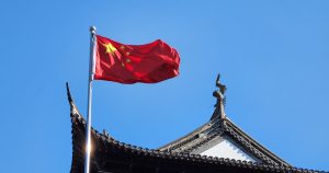 Flag of China, where a ruling on same-sex parents has been passed, flying on top of a building with a blue sky in the background.