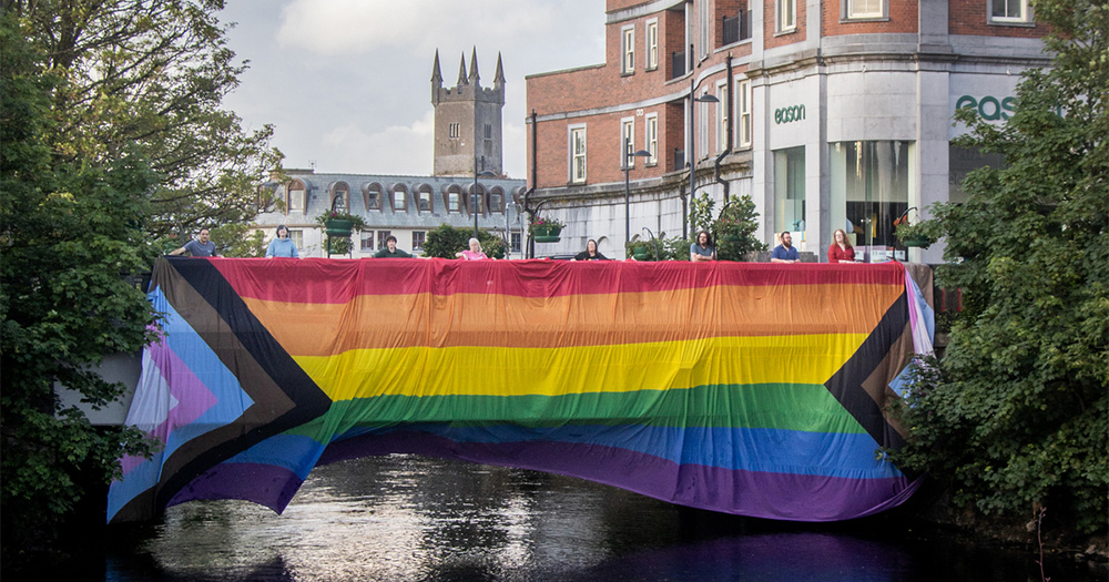 Image shows participants of last years Clare pride parade celebrating by holding a pride flag togther.