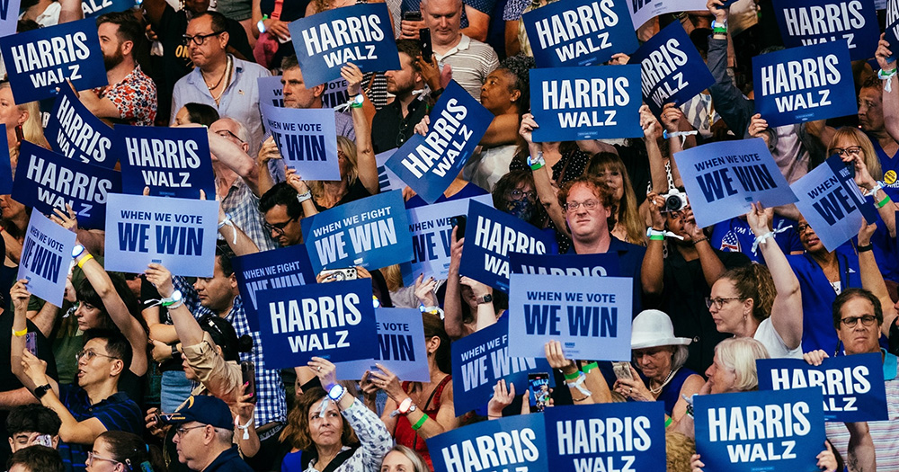 Image of Democrats supporters holding up signs reading 'Harris Walz' and 'We Win'.