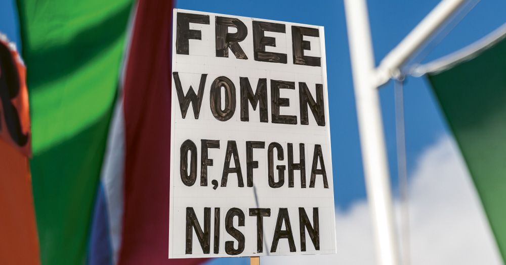 This article is about an LGBTQ+ refugee who left Afghanistan for Ireland. The image shows a sign that reads: "Free women of Afghanistan".