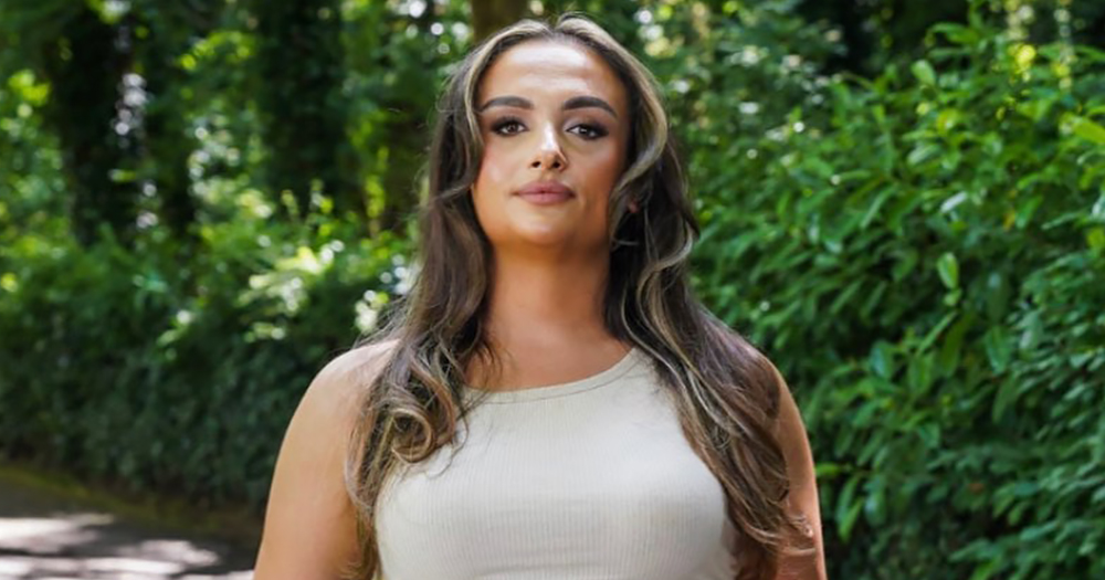 Photo of Paige Behan, a trans woman who was refused treatment at a hospital in Dublin, looking at the camera with nature in the background.