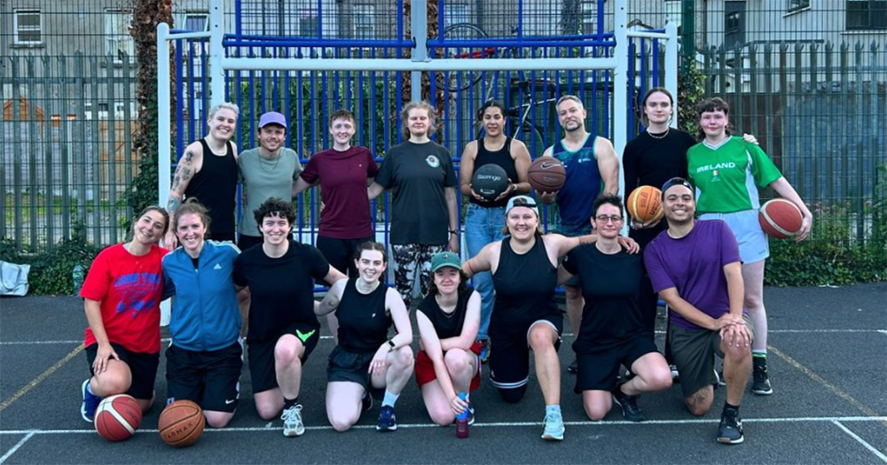 An image of Shamrock Síoga, Ireland's first LGBTQ+ basketball team. There are two rows of people, the front are kneeling and the back are standing. They are in an outdoor basketball court.