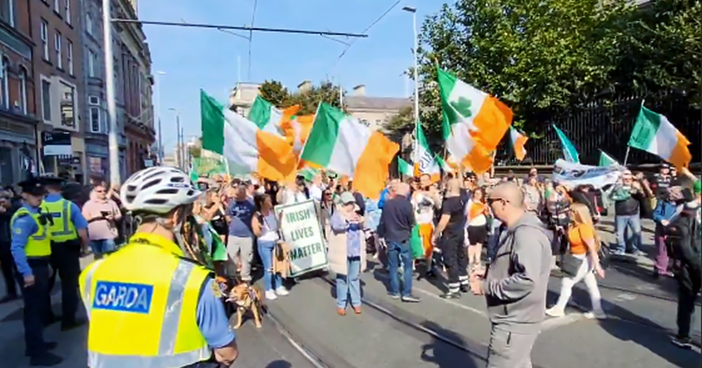 Anti-immigration protest taking place in Dublin, with a group of people waving Irish flags and Gardai