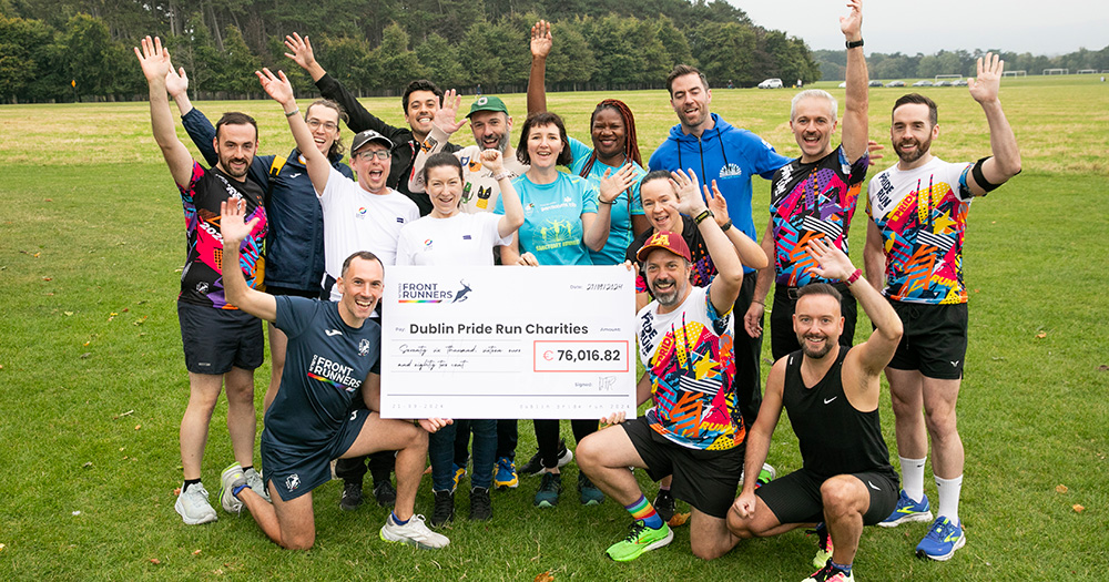 Member of the Dublin Front Runners celebrating raising €76,000 for charities from the 2024 Dublin Pride Run. A group of people hold a large cheque with the figure, and raise their arms in the air in celebration.