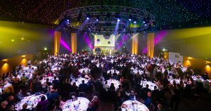 Photo from the last year's GALAS, with a few tickets left on sale. The room is lit up with colourful lights and people sitting around round tables.