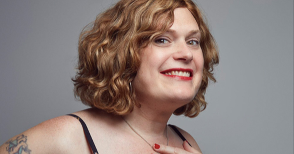 Filmmaker Lilly Wachowski, who will co-produce the film adaptation of a fantasy novel, smiling at the camera with a grey background.