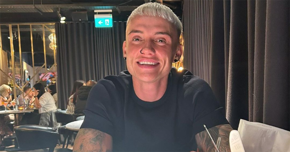 Married at First Sight UK contestant Eve smiles for a photo in a restaurant. She wears a black t-shirt and sits at a table. She has bleach blonde short hair.