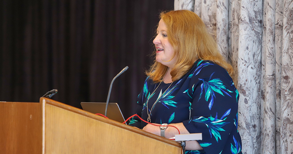 Northern Irish Justice Minister Naomi Long, who has vowed to introduce hate crime legislation to the Assembly. She speaks at a podium, wearing a blue patterned top.