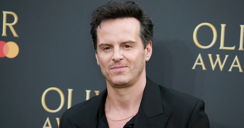 Andrew Scott, who will star in a new sci-fi romance, on a red carpet with a black background, smiling at the cameras.