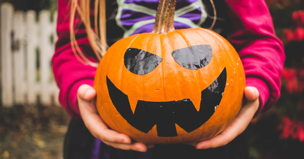 This article is about Halloween events organised by Belong To. In the photo, the hands of a young person holding a carved pumpkin.