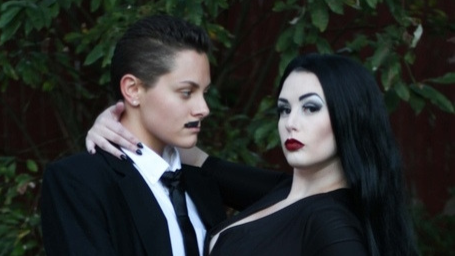 This queer couple costume idea for Halloween is The Addams Family themed, so pictured are two people dressed as Morticia and Gomez Addams, wearing black and white.