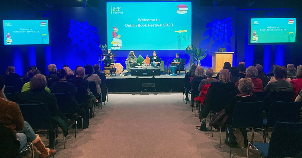 Photo taken at the Dublin Book Festival, with people in the audience listening to people talk on a stage.