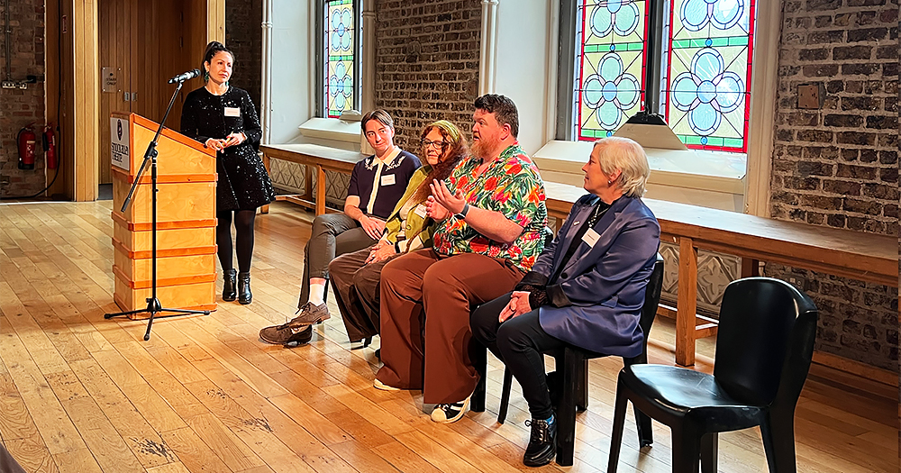 Panel of speakers at the launch of EMBER, a guide for LGBTQ+ people about addressing their end-of-life needs. The speakers are sitting on chair while speaking to the audience.