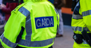 This article is about a man arrested for spreading false claims online. In the photo, the back of a Garda in a yellow uniform.