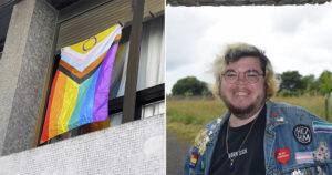 This is an article on how to find LGBTQ+-friendly housing in Ireland amidst the housing crisis. The picture shows a young gay trans man, Miles, smiling. He is wearing glasses and a denim jacket with many patches on it. The other half of the picture shows a prideflag hanging from a window.