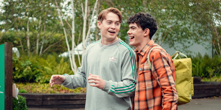 The first idea for a queer couple costume for Halloween is from Heartstopper. In the picture, Nick and Charlie are standing next to each other laughing. Nick is wearing a grey sweatshirt with green stripes and Charlie an orange shirt. 