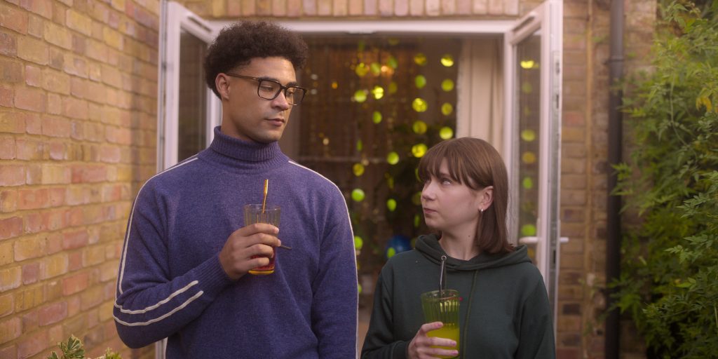 Screenshot from Heartstopper TV show. It shows the characters of Michael and Tori looking at each other while holding a glass.