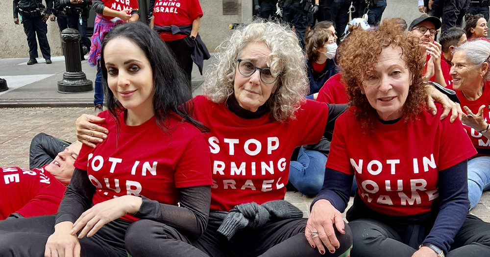 Nan Goldin, Debra Winger and Molly Crabapple at a pro-palestine protest, sitting on the floor and wearing red t-shirts with the messages: Stop arming Israel.