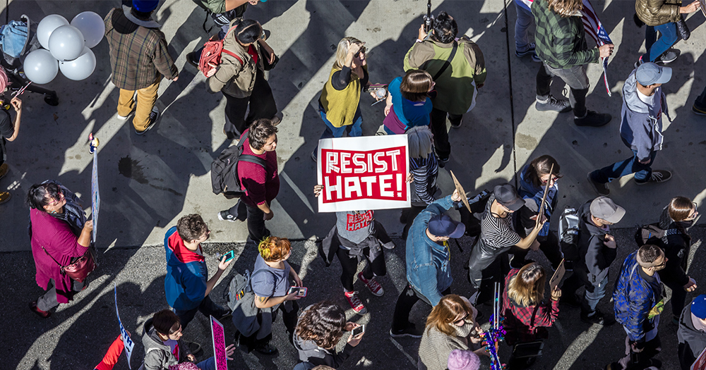 This article is about anti-LGBTQ+ attacks in Ireland. In the photo, people walking on a street withe one person holding a sign that reads "resist hate".