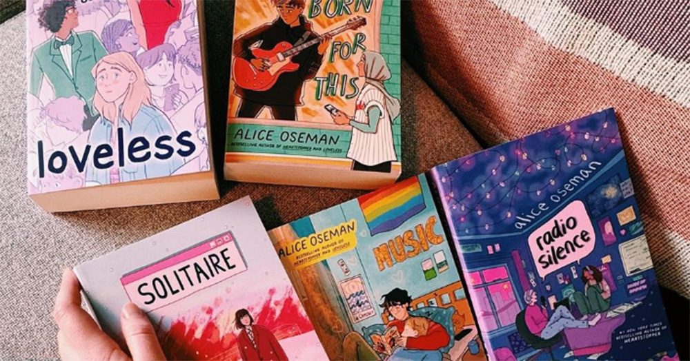 An image of some of the graphic novels from the Heartstopper universe lying on a bed.