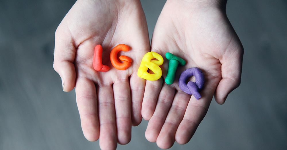 This article is about different LGBTQ+ identities. The image shows hands holding the letters LGBTQ+ made out of clay.