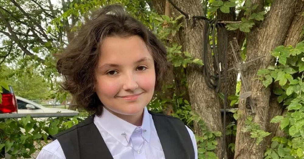 Photo of Nex Benedict, a trans teen who attented an Oklahoma school, smiling at the camera with trees in the background.