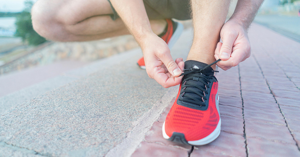 This article is about a HIV awareness run. The image shows a person kneeling down to tie their shoe lace on a pair of red runners.